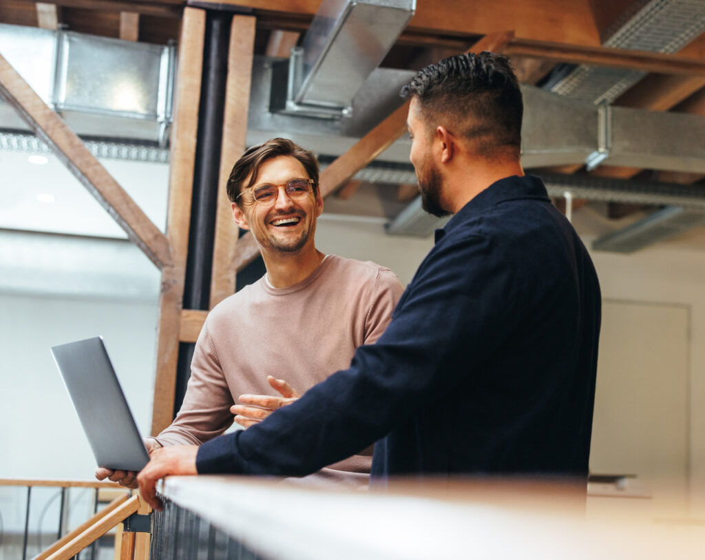 Zwei Geschäftsleute im Gespräch über ihre Tech-Arbeit, gestikulierend und fokussiert in einem modernen Büro.