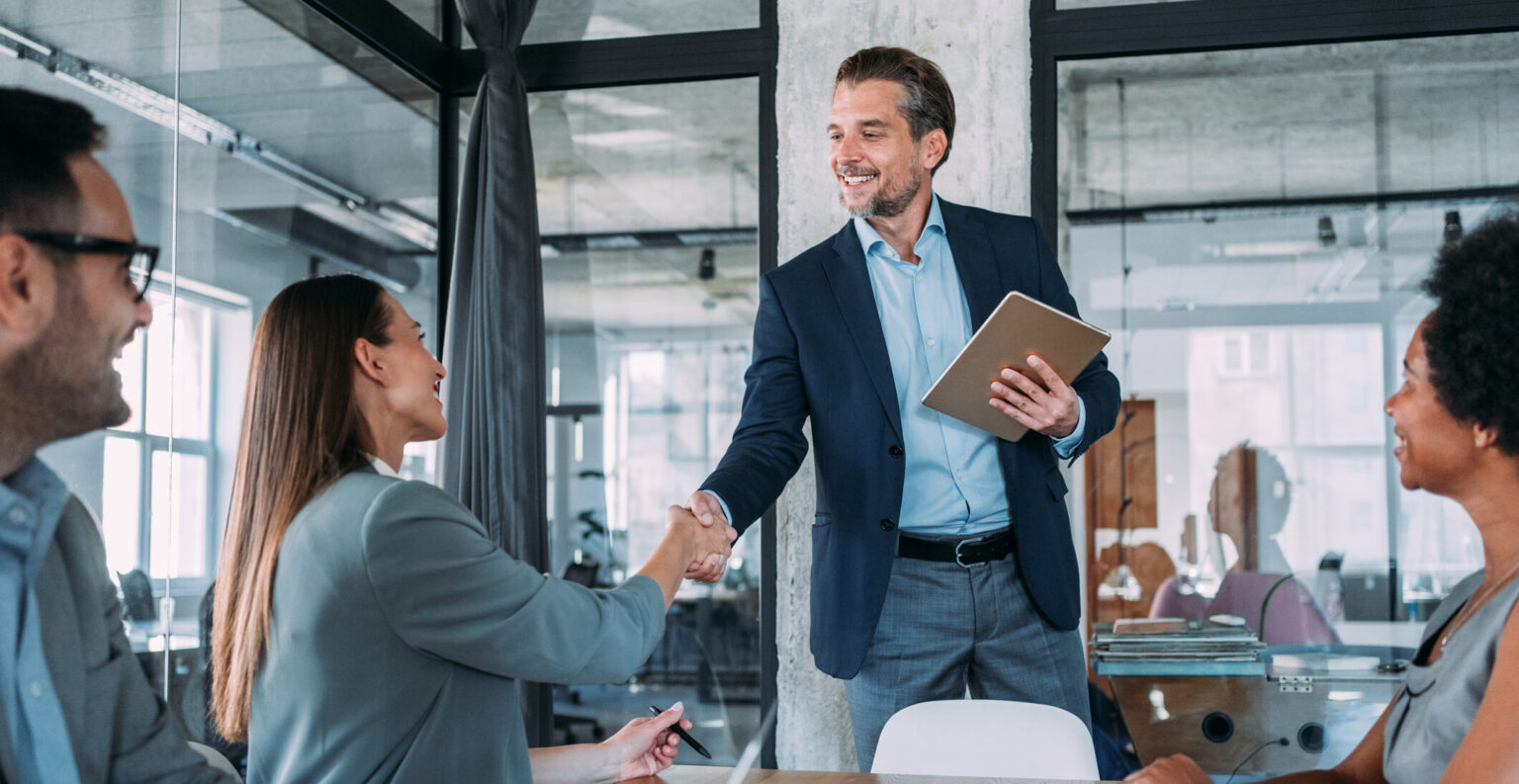 Geschäftsfrau und Geschäftsmann schütteln sich über den Tisch die Hände, symbolisieren erfolgreiche Zusammenarbeit und Einigung.