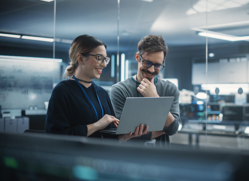 Two engineers collaborate on a laptop, discussing ideas and analyzing technical plans in a modern office.